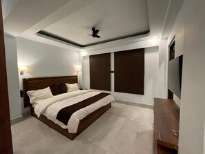 A modern bedroom with a large bed, a ceiling fan, and a TV on the right. - Blue Angel Annexe (Shillong)
