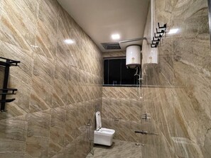 A modern bathroom with a marble floor and walls, a white toilet, a shower area, and a towel rack. - Blue Angel Annexe (Shillong)
