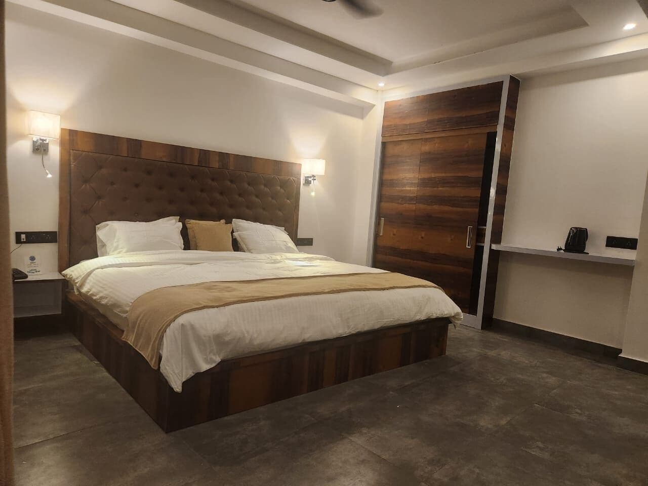 A modern bedroom with a large bed, wooden headboard, bedside lamps, and a wardrobe.