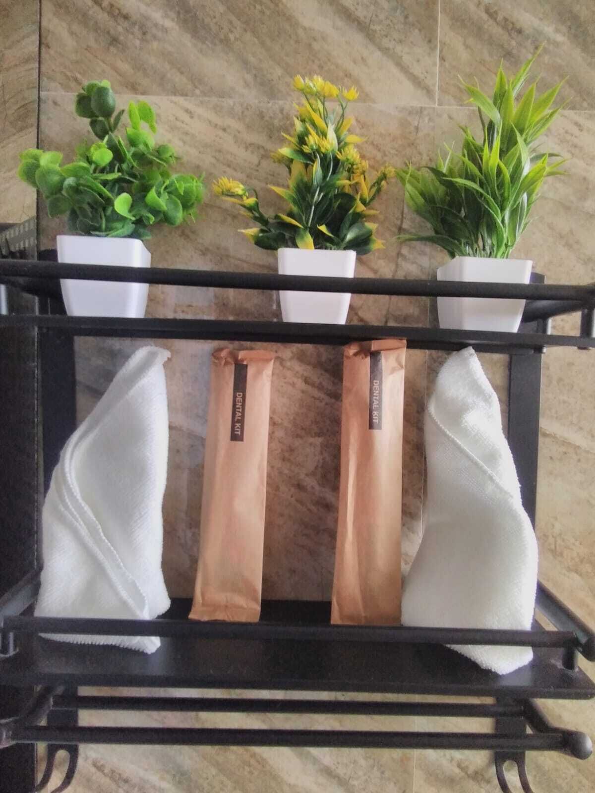 Una estantería de metal negro con tres macetas blancas que contienen plantas verdes y dos bolsas de papel marrón con la etiqueta 'DENITAL KIT'.