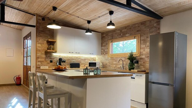 A modern kitchen with a central island, white cabinetry, a stainless steel refrigerator, and pendant lighting.