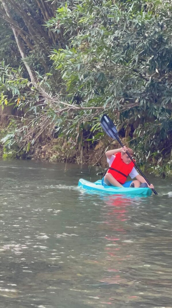 A person kayaking in a river surrounded by dense foliage.