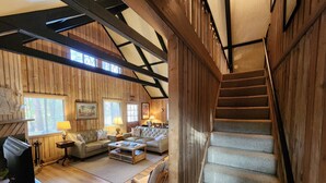 Un salon chaleureux avec une cheminée, des murs en bois, un escalier et une vue sur l’extérieur.