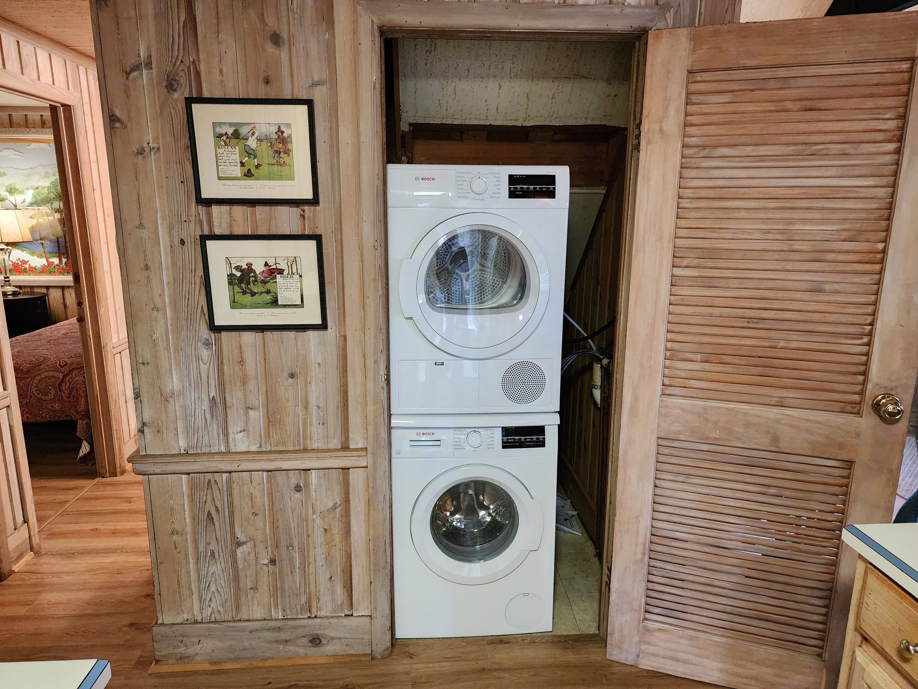 A laundry room with a Bosch washing machine and dryer, wooden walls, and framed pictures.