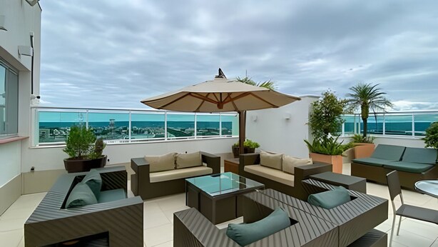 A rooftop terrace with outdoor seating, a large umbrella, and a view of the sea. - OZPED Flats Particulares Biarritz (Brasília)