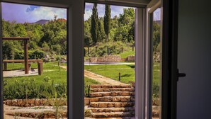 A view through a window of a stone staircase leading to a grassy area with a wooden pergola and a stone wall.