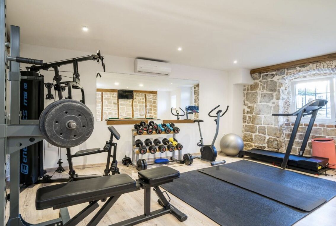 Ein Heimfitnessraum mit einer Hantelbank, Kurzhanteln, einem Laufband und einem Ergometer.