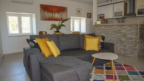 A modern living room with a gray sofa, yellow cushions, a colorful rug, and a dining area with a kitchen in the background.