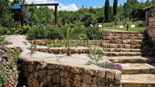 A stone staircase leading up to a wooden pergola, surrounded by a landscaped garden with various plants and flowers.
