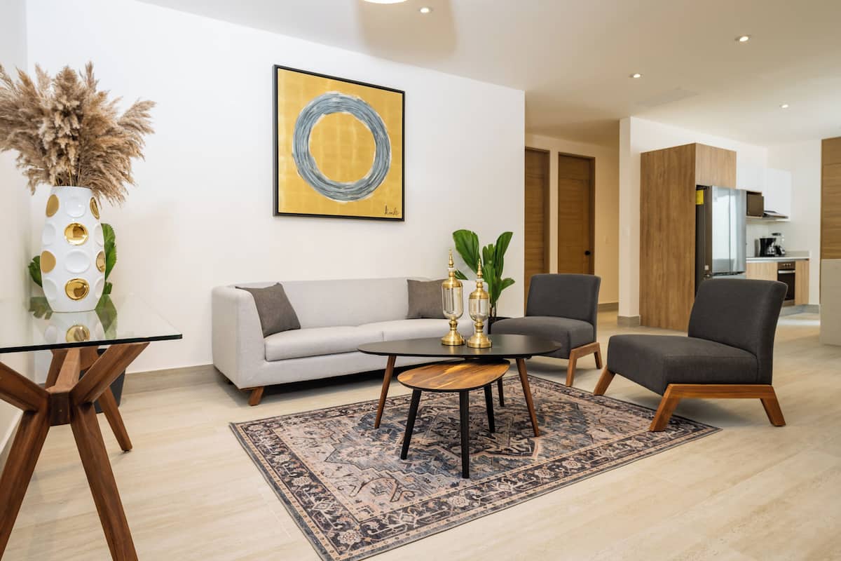 Een moderne woonkamer met een bank, twee fauteuils, een glazen salontafel en een decoratieve vaas.