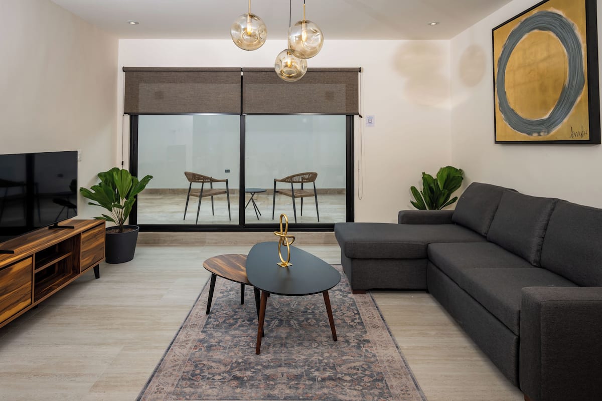Een moderne woonkamer met een hoekbank, een salontafel, een televisie en een groot raam met uitzicht.