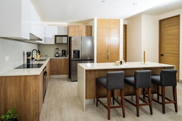 A modern kitchen with a central island, bar stools, wooden cabinets, and stainless steel appliances.