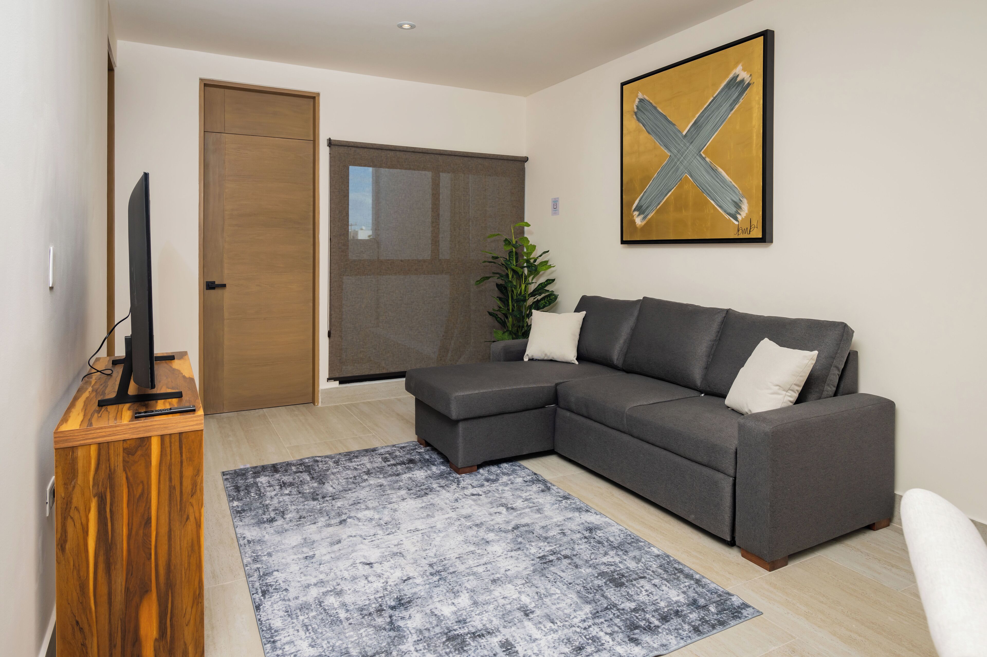 Een moderne woonkamer met een grijze modulaire bank, een houten tv-meubel, een groot abstract schilderij en een schuifdeur naar een balkon.