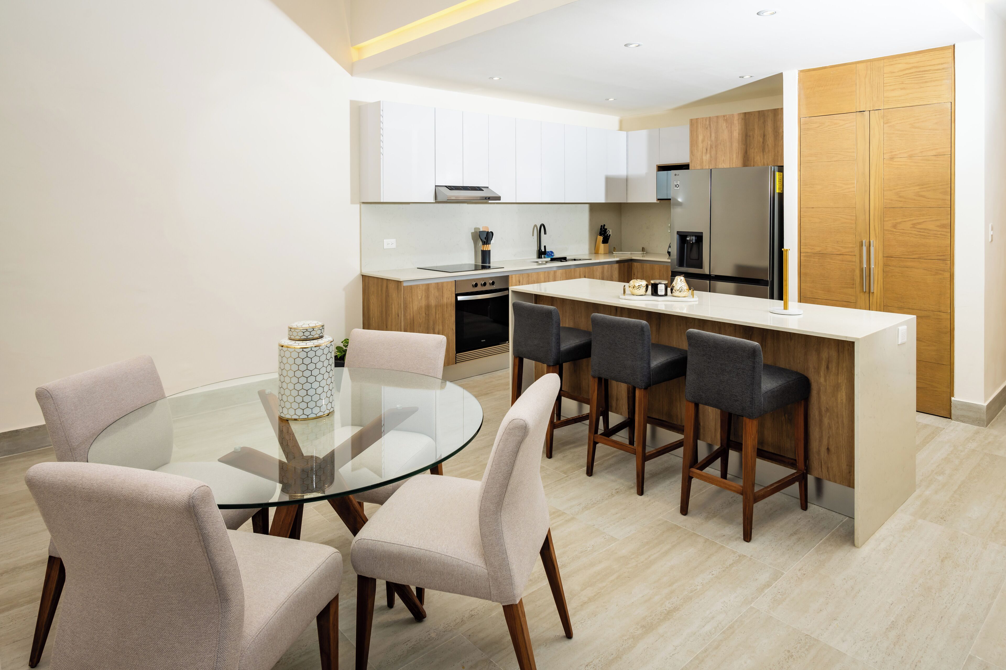 A modern kitchen with white cabinets, a central island with bar stools, and a glass dining table with four chairs.