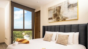 Habitación de hotel con una cama grande, vista a zonas verdes por la ventana y un cuadro abstracto moderno en la pared.