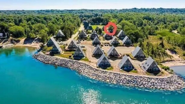 Un complex turístic costaner amb diverses cabanes de teulada triangular distribuïdes al voltant d'una zona central, comunicades per una riba rocosa.