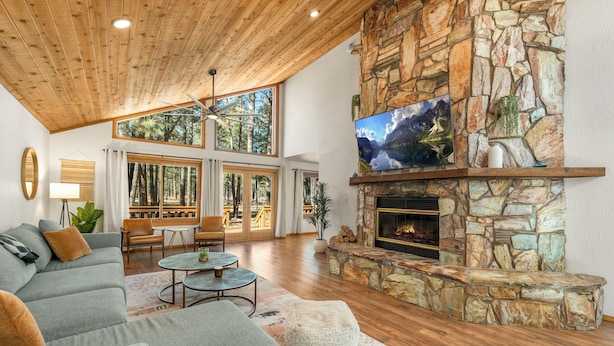 Un salón amplio con chimenea de piedra, un televisor grande montado encima y un rincón de descanso acogedor con sofá y sillones.