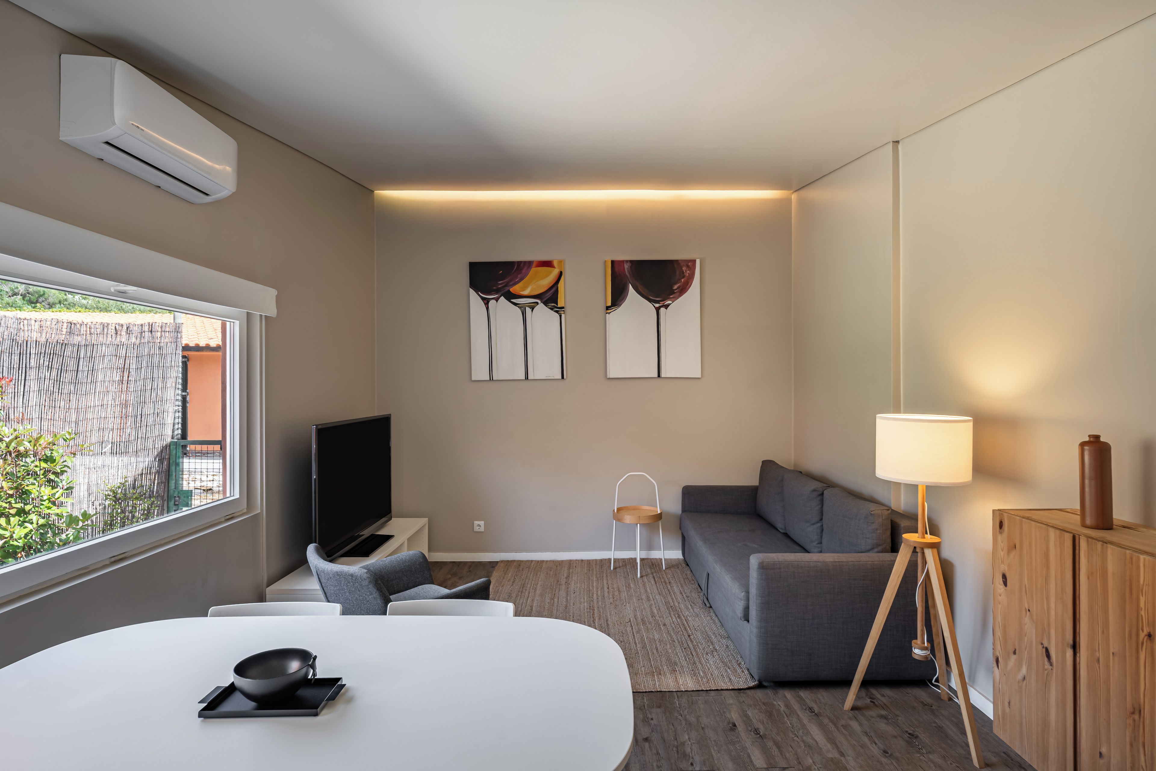 A modern living room with a flat-screen TV, grey sofa, and a dining table with a bowl.