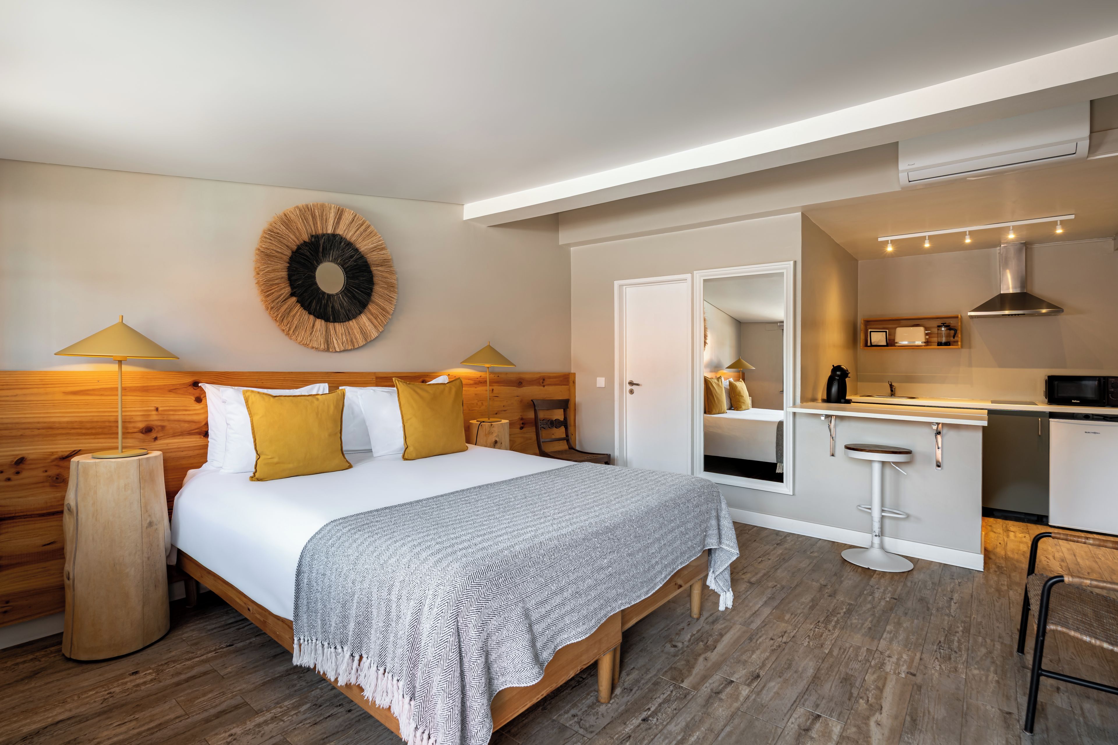 A modern bedroom with a wooden headboard, a large bed with a patterned throw, two bedside lamps, and a wall-mounted circular decoration.