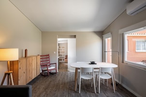 Una habitación compacta con una mesa redonda y sillas, un armario de madera, una silla roja y una ventana con vistas.