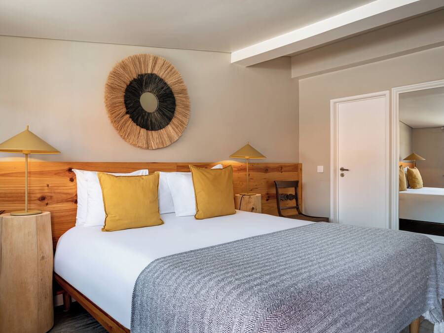 Un dormitorio con cabecera de madera, decoración circular en la pared, dos lámparas de noche y una cama con almohadas blancas y mostaza.