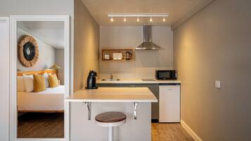 A compact kitchen with a white countertop, a built-in microwave, a coffee maker, and a small refrigerator.