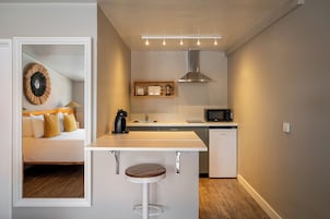 Cocina compacta con encimera blanca, microondas integrado, cafetera y refrigerador pequeño.