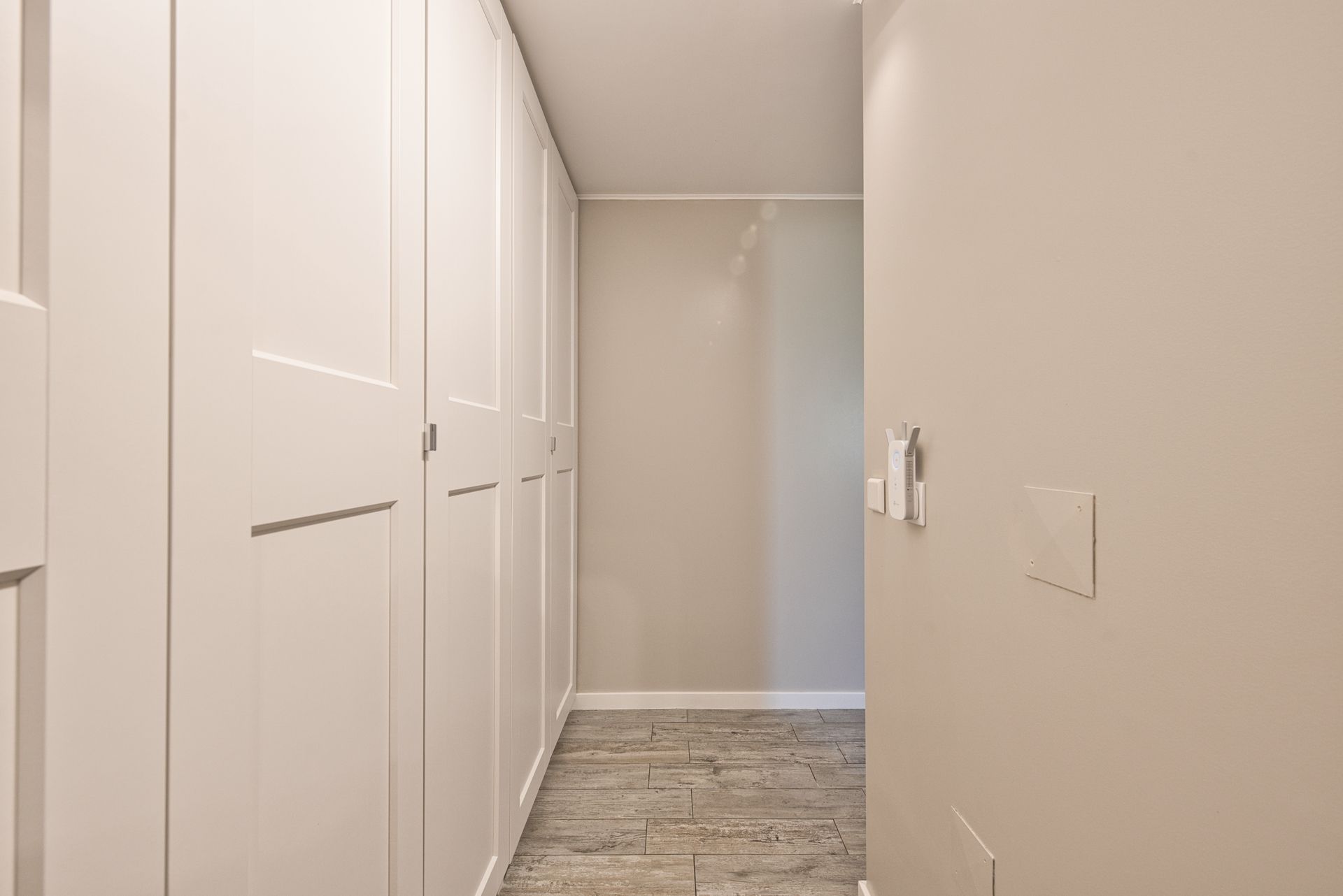 A narrow hallway with white doors, a wooden floor, and a light switch on the wall.