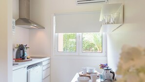 A compact kitchen with white cabinetry, a built-in stove, and a window providing a view of greenery outside. - Quinta da Bicuda (Cascais)