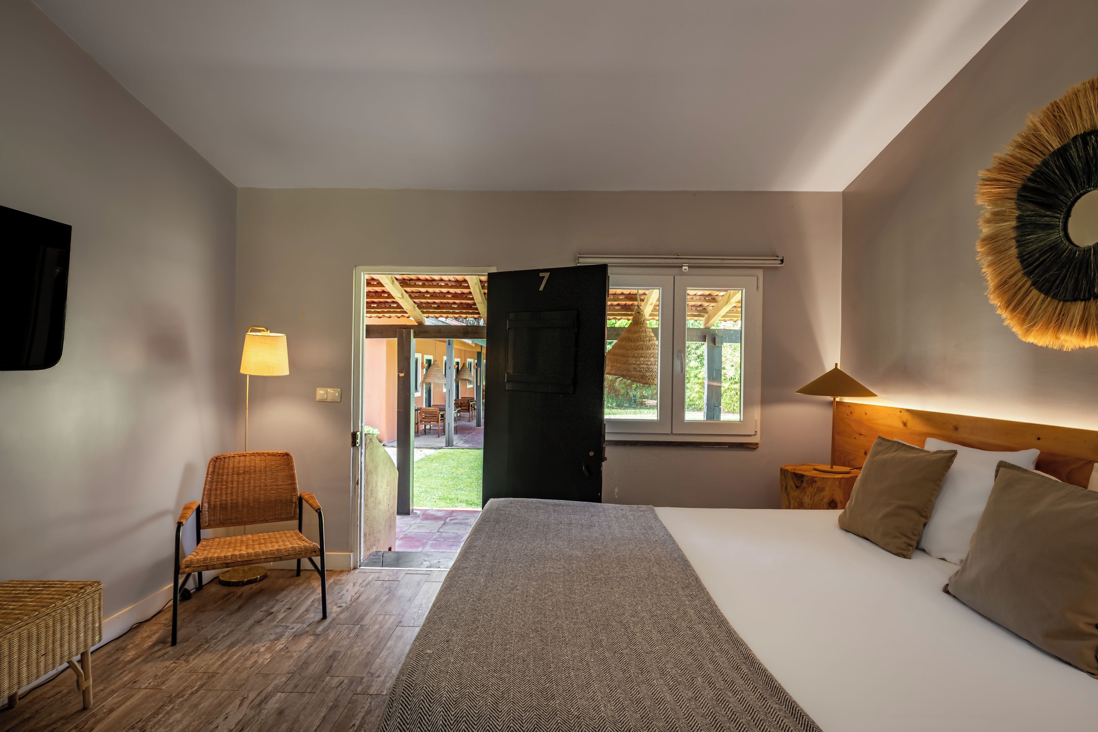 A bedroom with a bed, a chair, a lamp, and a view of an outdoor area.