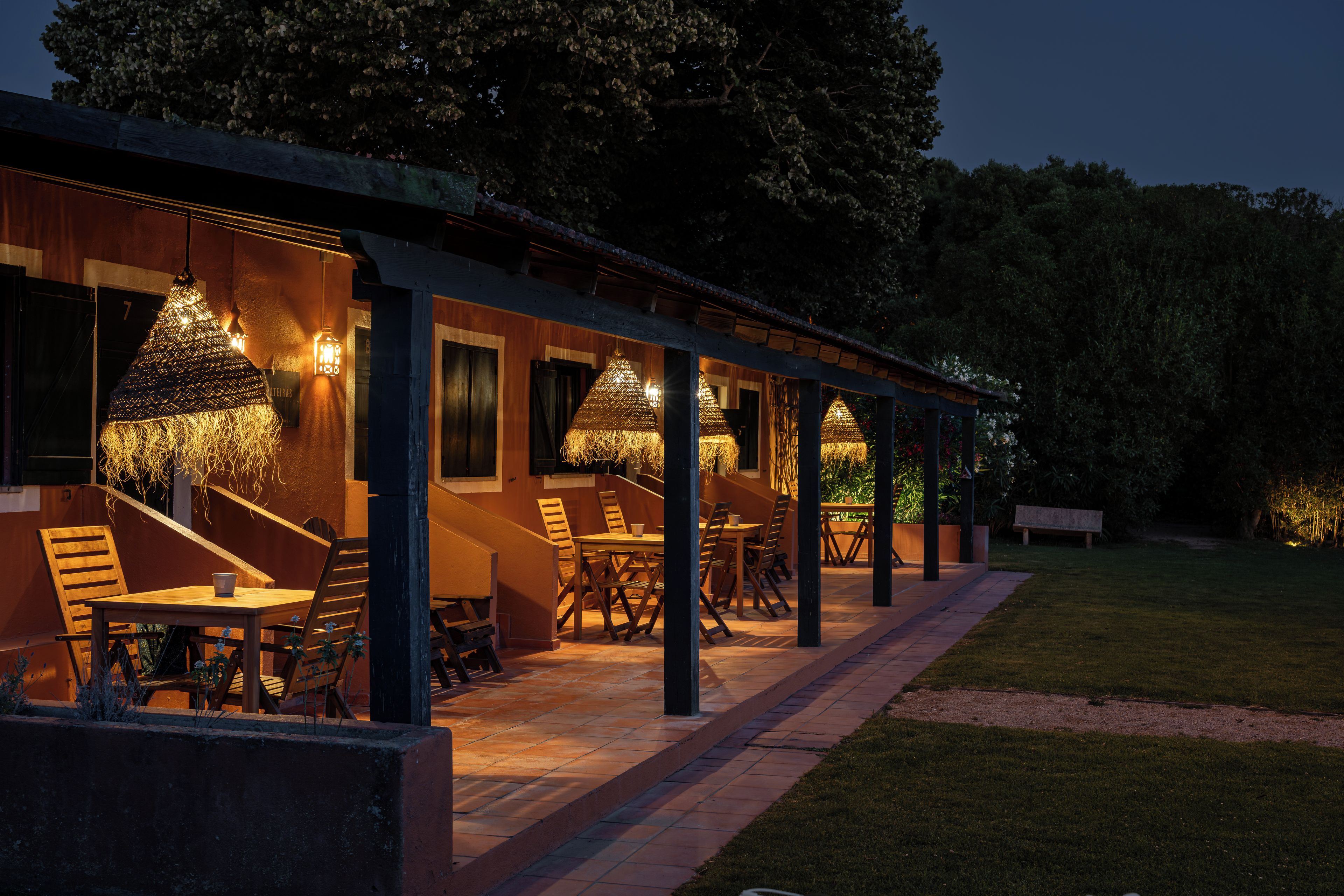 An outdoor dining area with tables and chairs, surrounded by a covered walkway with hanging lights.