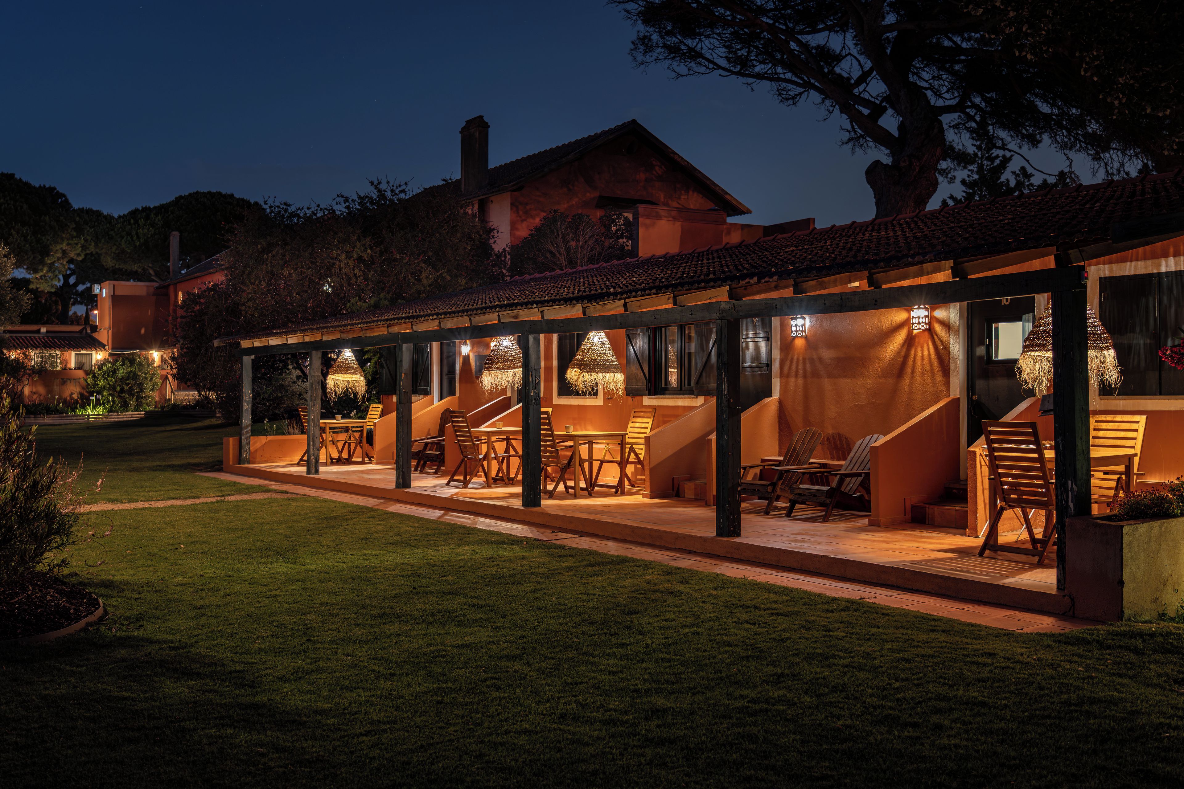 A covered outdoor seating area with tables and chairs, a staircase, and a view of the surrounding landscape.