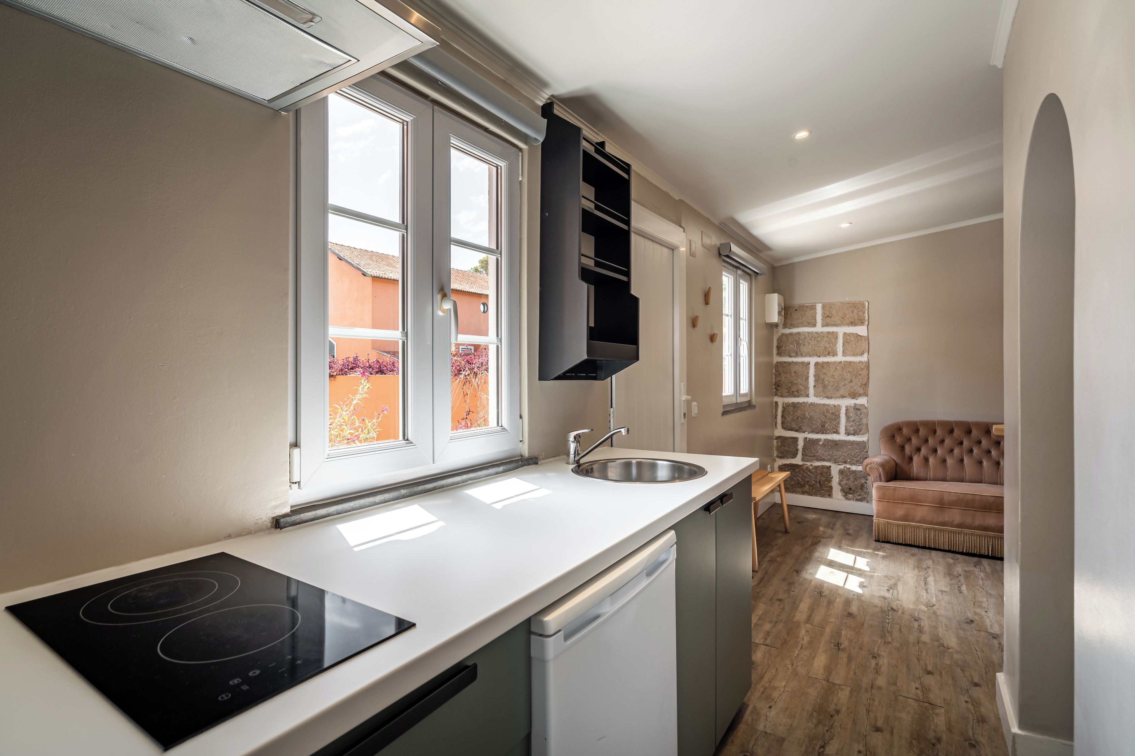 A compact kitchen with a dishwasher, a built-in oven, and a window overlooking a garden.