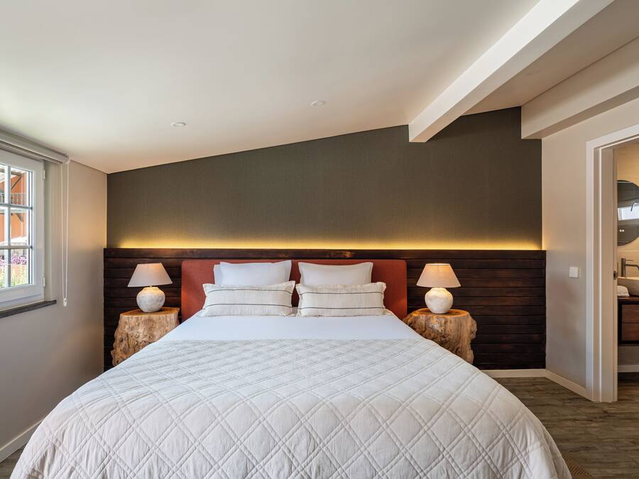 Habitación de hotel con una cama grande, dos mesitas de noche con lámparas, un cabecero de madera y vistas al baño.