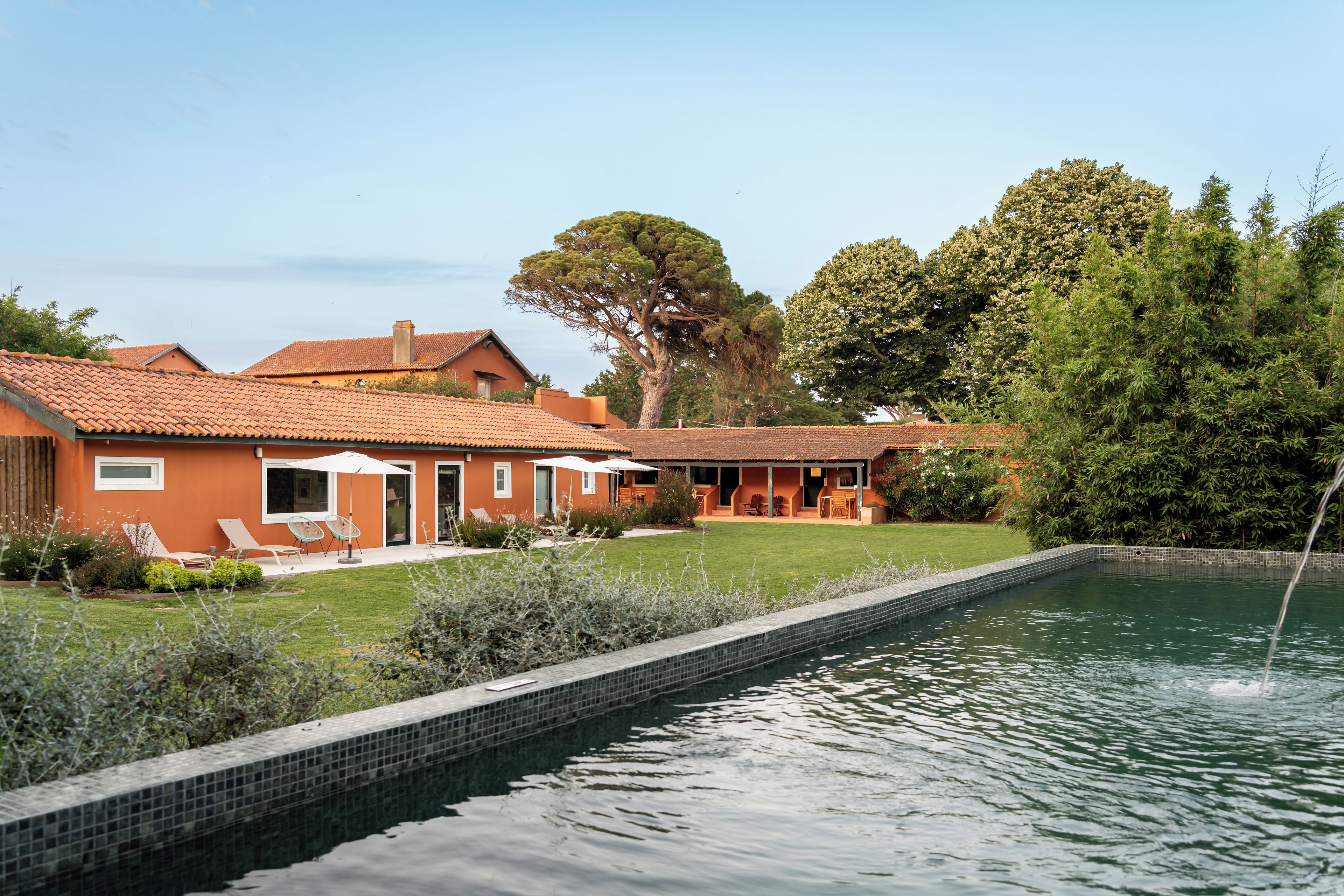 Una casa con piscina, mobiliario exterior y un gran árbol.