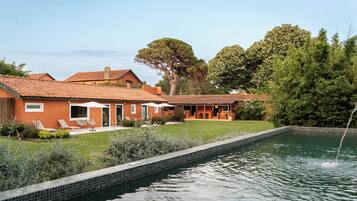 Una casa con piscina, mobiliario exterior y un gran árbol.
