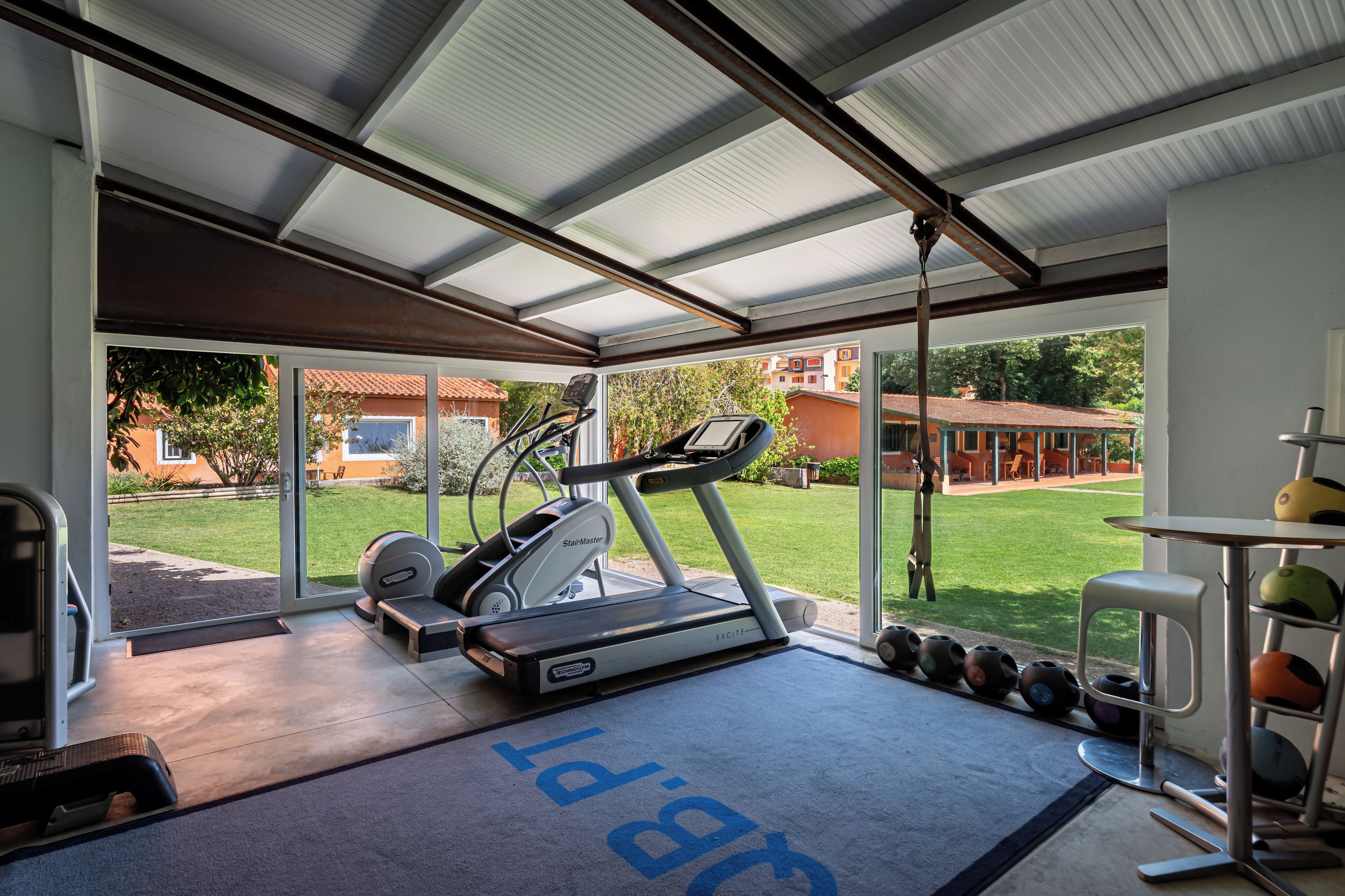 A gym with a treadmill, weights, and a covered area with a view of a residential area.