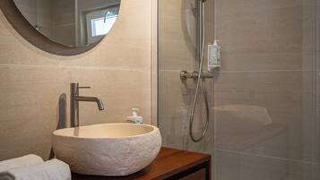 A bathroom with a round mirror, a vessel sink, a wooden vanity, and a glass-enclosed shower area.