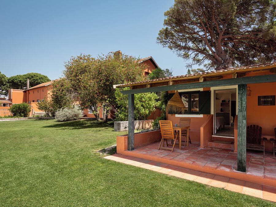 A covered outdoor seating area with a table and chairs, a small garden, and a building with a tiled roof.