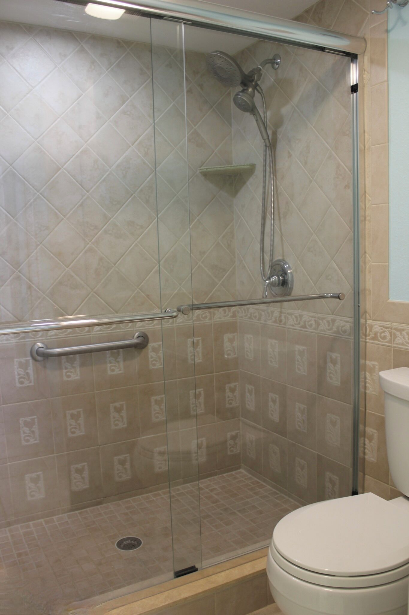 A glass-enclosed shower with a handheld showerhead and a handheld faucet.