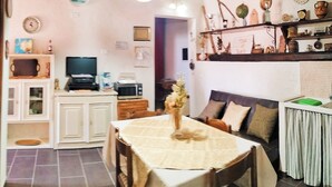 Un coin repas avec une table dressée pour quatre personnes, un téléviseur et un espace cuisine équipé de placards et d’un four à micro-ondes.