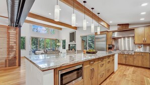 Eine moderne Küche mit Holzschränken, Edelstahlgeräten und großen Fenstern.