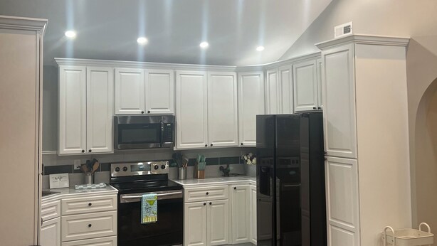 Una cocina moderna con armarios blancos, electrodomésticos de acero inoxidable y un ventilador de techo.