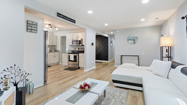 A modern living room with a white sofa, a coffee table, and a kitchen in the background. - Charming 4-bedroom bungalow with AC and WiFi in Hampton, with washer and dryer. (Hampton)