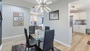 A modern dining area with a glass table and black chairs, a contemporary chandelier, and framed artwork on the walls. - Charming 4-bedroom bungalow with AC and WiFi in Hampton, with washer and dryer. (Hampton)
