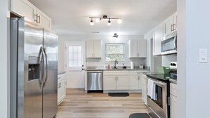 A modern kitchen with stainless steel appliances, white cabinetry, and a wooden floor. - Charming 4-bedroom bungalow with AC and WiFi in Hampton, with washer and dryer. (Hampton)