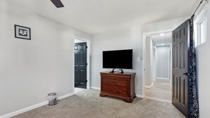 A hallway with a wooden dresser, a television on top, and a door leading to another room. - Charming 4-bedroom bungalow with AC and WiFi in Hampton, with washer and dryer. (Hampton)