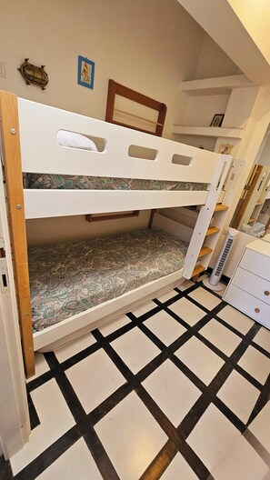 Una cama litera con colchón estampado, un estante con un marco de fotos y un calentador en el suelo.