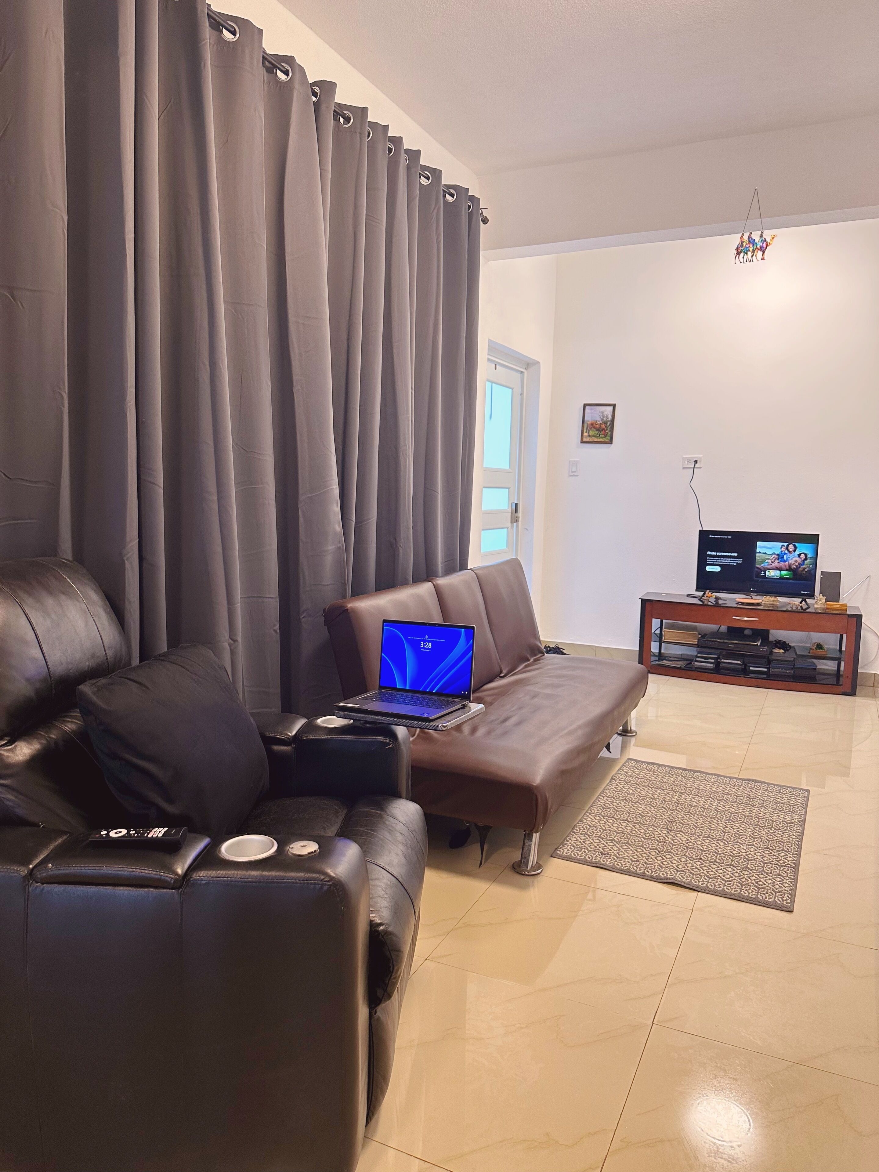 A living room with a sofa, a coffee table, a laptop, a television, and a small cabinet.