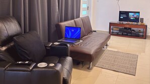 Ein Wohnzimmer mit einer Couch, einem Couchtisch, einem Laptop, einem Fernseher und einem kleinen Schrank.